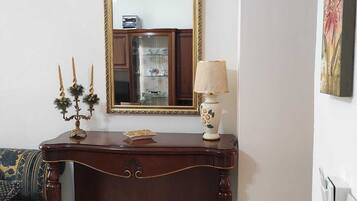 Une console en bois foncé, surmontée d’un miroir, avec une petite figurine de chien blanc et une lampe posée sur le plateau.