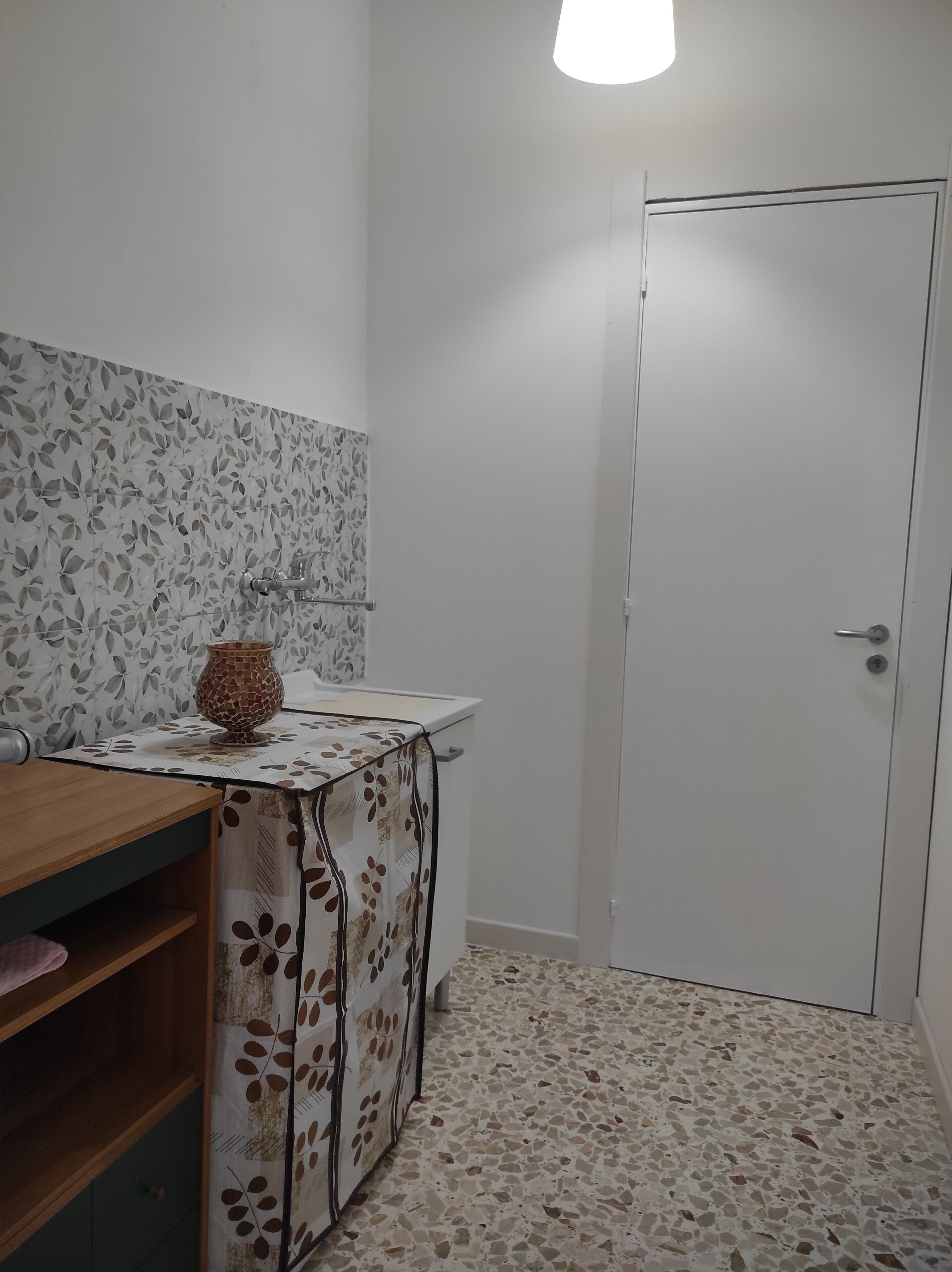 Un bany amb terra de rajola, un penjador de fusta amb mirall, un rentapeus i un vas decoratiu.