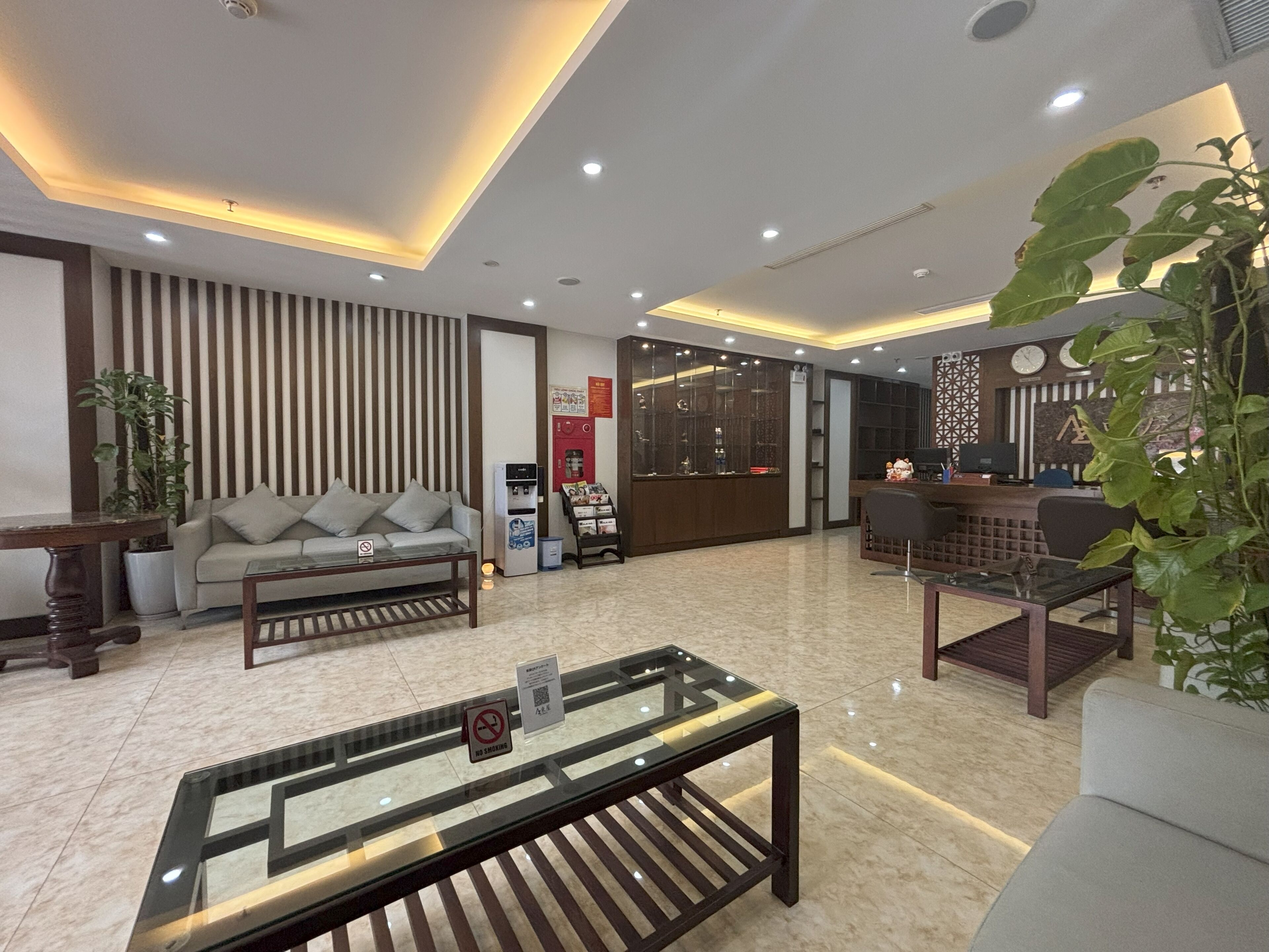 A modern hotel lobby with a sofa, a coffee table, a reception desk, and a large plant.