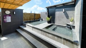 Un área de spa moderna al aire libre con dos jacuzzis, una cubierta de bambú y vistas a la ciudad.