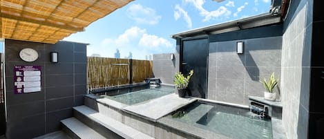 Ein moderner Wellnessbereich im Freien mit zwei Whirlpools, einer Bambus-Überdachung und Blick auf die Stadt.