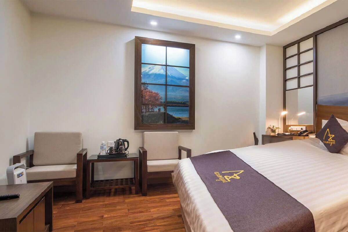 A hotel room with a bed, a desk, a chair, a painting, and a view of a mountain.