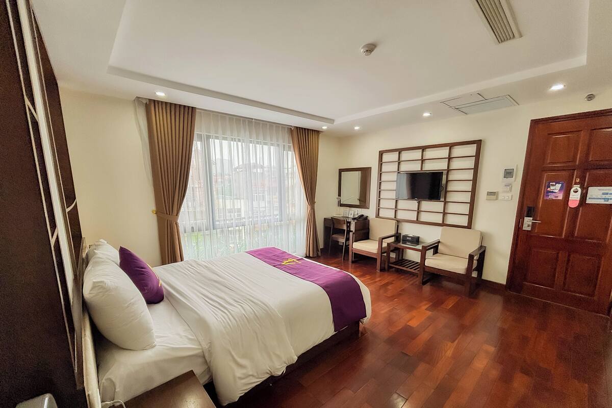 A hotel room with a bed, a desk, a chair, a television, and a door.