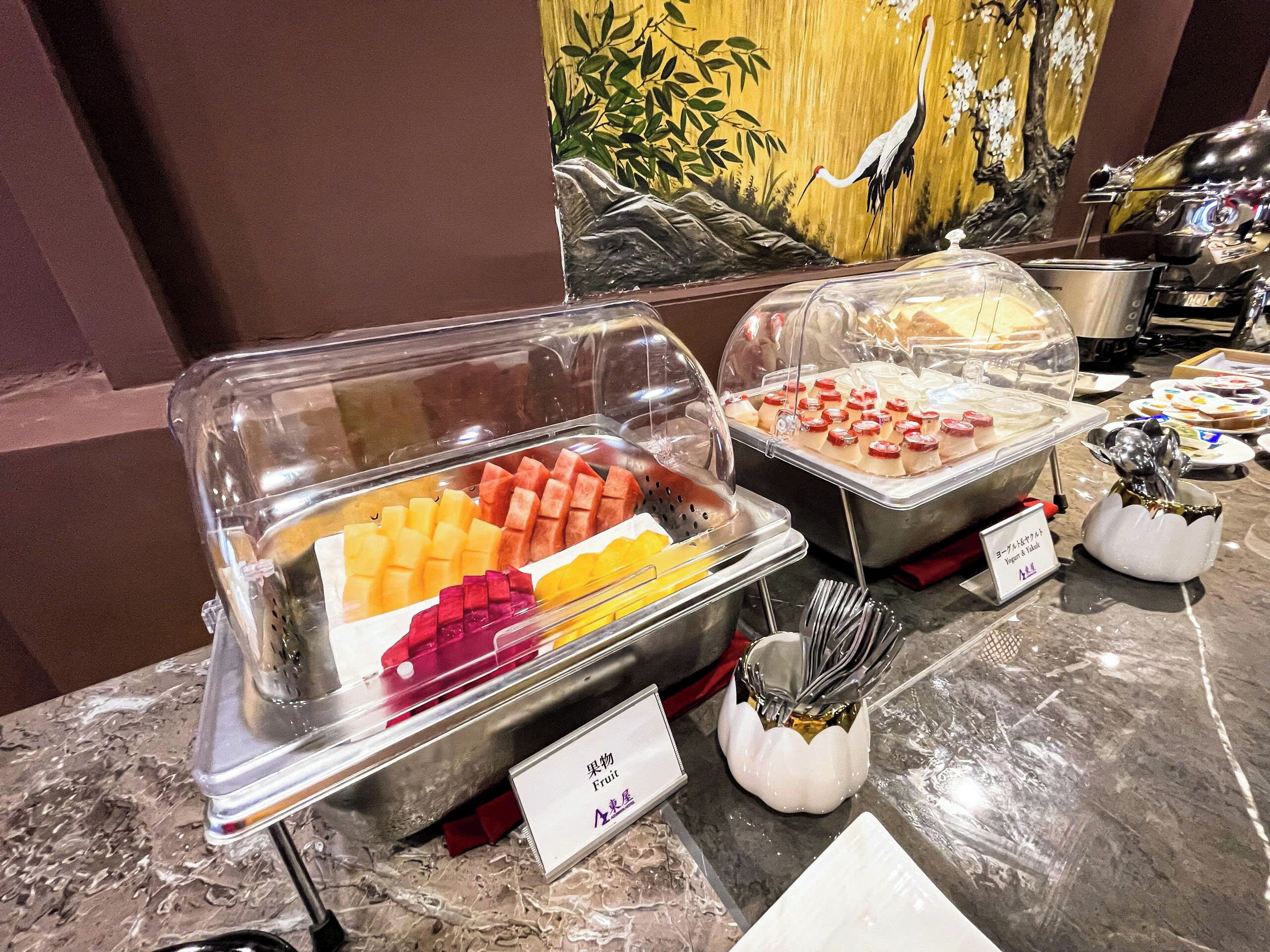 Un buffet con diversi tipi di frutta e un cartello che indica la presenza di yogurt e parfait di yogurt.