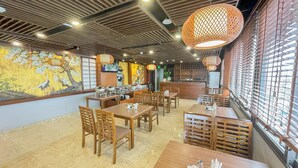 A restaurant with wooden tables and chairs, a buffet setup, and a mural on the wall. - Azumaya Hotel Dao Tan (Hanoi)