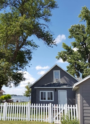 Une maison à deux étages avec une clôture en bois peinte en blanc, une façade grise et une petite fenêtre au deuxième étage.