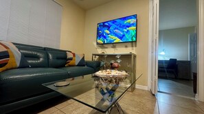 Un salon avec un canapé en cuir vert, une table basse en verre et un téléviseur à écran plat qui diffuse des images de poissons aux couleurs vives.