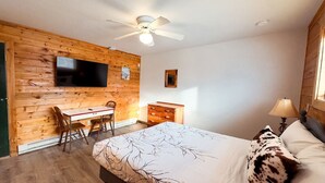Ein Schlafzimmer mit Bett, Schreibtisch, Stuhl, Kommode und einem an der Wand befestigten Fernseher.