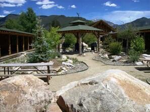 En stuga med träkonstruktioner, picknickbord och en central pergola.