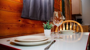 A dining table set with plates, a wine glass, and a small potted plant, with wooden paneling and a curtain in the background.