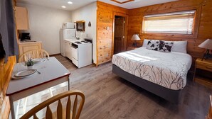 A compact room with a bed, a small kitchenette, a dining table, and a ceiling fan.