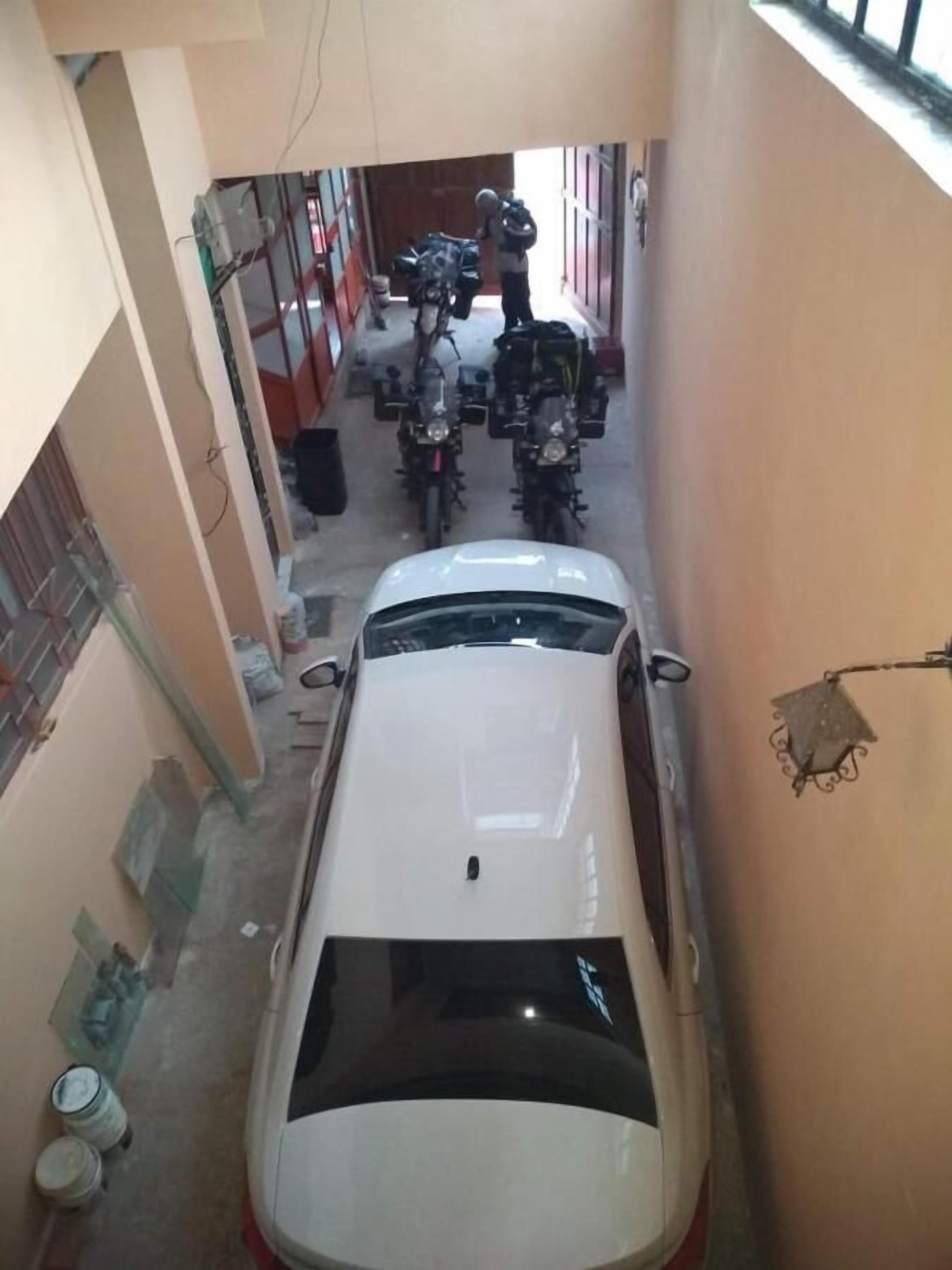 Un callejón estrecho con un coche blanco estacionado a la derecha, una motocicleta a la izquierda y una persona cerca de las motocicletas.