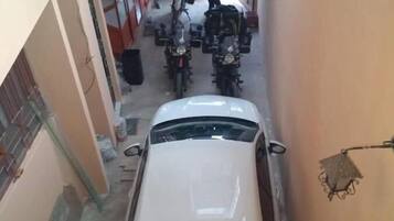 Un callejón estrecho con un coche blanco estacionado a la derecha, una motocicleta a la izquierda y una persona cerca de las motocicletas.