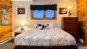A bedroom with a bed, a nightstand, a dresser, a window with a view, and a quilt. - Cozy Cabin 1 Block to Lake/In Town/Hummingbird (Grand Lake)