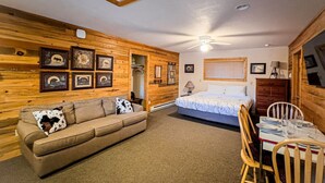 A cozy room with a wooden wall, a bed, a sofa, and a dining table with chairs. - Cozy Cabin 1 Block to Lake/In Town/Hummingbird (Grand Lake)