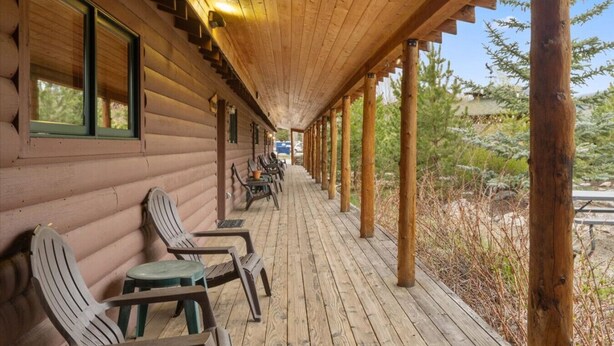 A log cabin with a covered porch, wooden chairs, and a view of the surrounding forest. - Cozy Cabin 1 Block to Lake/In Town/Hummingbird (Grand Lake)