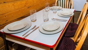 Een eettafel gedekt met borden, bestek en glazen, met een houten wand en een stoel op de achtergrond.