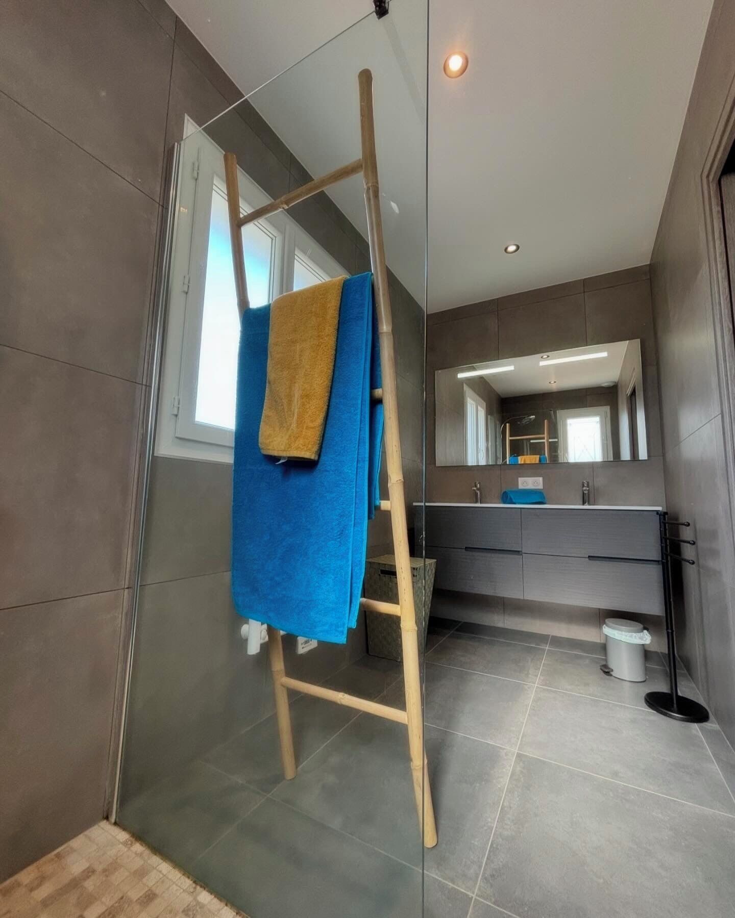 Une salle de bain moderne avec une douche à parois de verre, une échelle en bois et une serviette bleue suspendue à celle-ci.