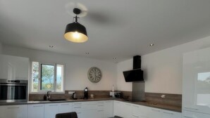 A modern kitchen with a wooden dining table, white cabinets, and a black ceiling fan. - Villa Melendria, Ghisonnaccia (Ghisonaccia)