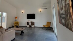 A spacious living room with a large flat-screen TV mounted on the wall, a modern sofa, a coffee table, and two chairs. - Villa Melendria, Ghisonnaccia (Ghisonaccia)