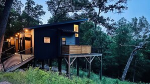 Een boomhut met een houten terras, een trap en een klein raam.