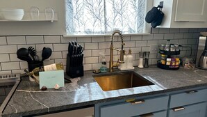Een keuken met een granieten aanrecht, een roestvrijstalen spoelbak en een raam met uitzicht op kale bomen.