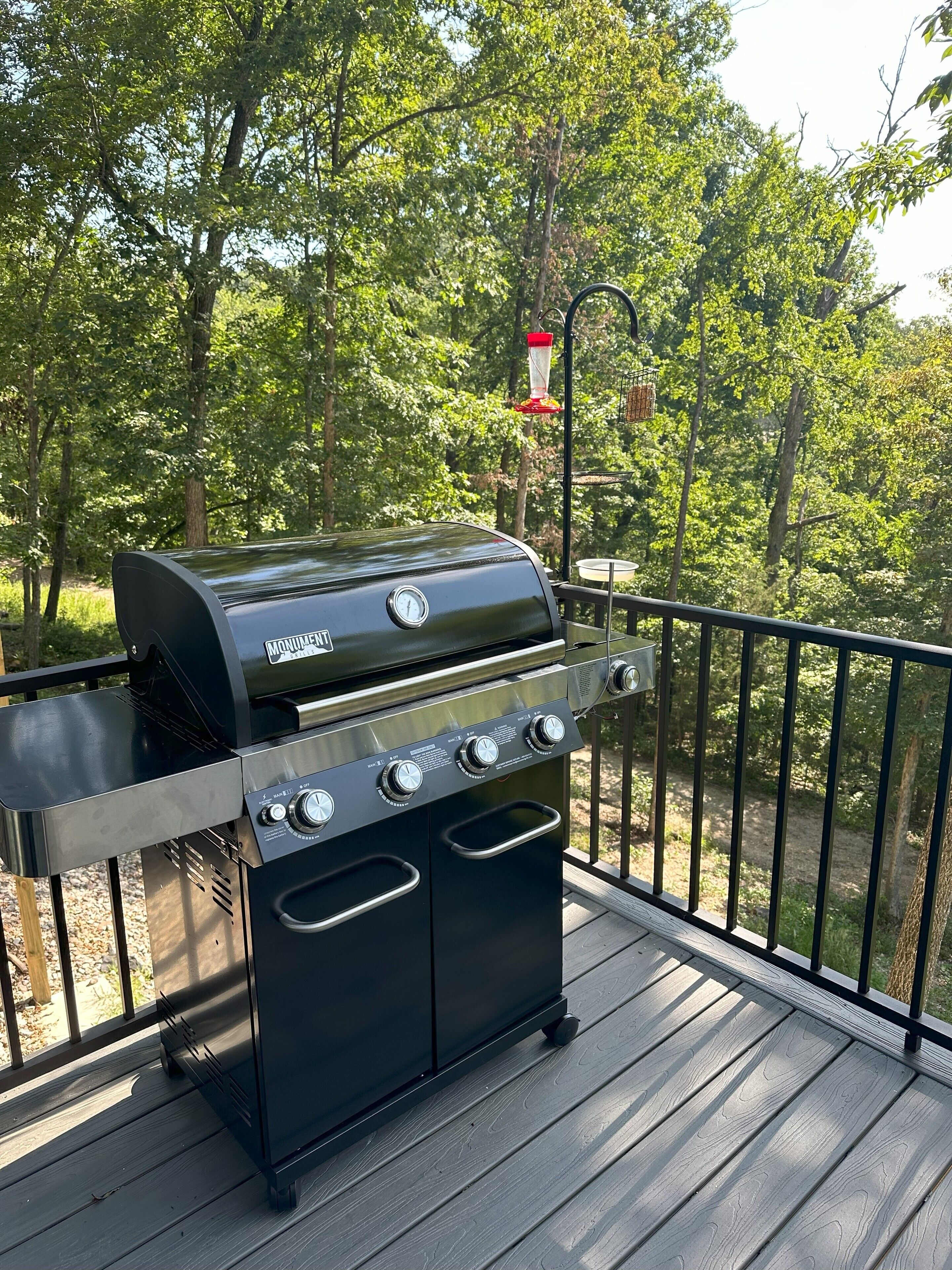 A black outdoor grill with four burners and a side cabinet, located on a wooden deck with a metal railing.