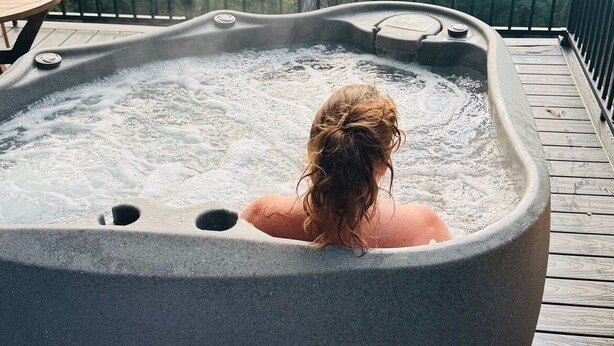 Een hottub op een houten terras met uitzicht op een bos.