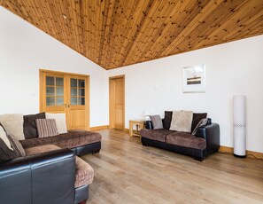 A spacious living area with wooden flooring, two sofas with cushions, a wooden ceiling, and a framed picture on the wall.
