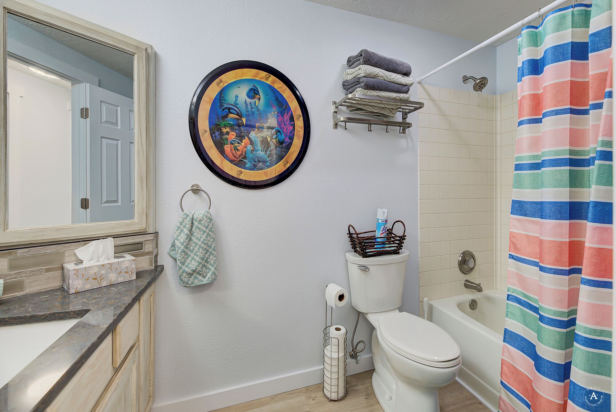 A bathroom with a toilet, a bathtub, a shower curtain, a towel rack, a toilet paper holder, and a decorative plate on the wall.