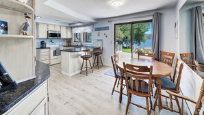 A modern kitchen with a central island, wooden dining table, and chairs. - Lakefront single story house on Hauser Lake (Helena)