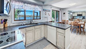 A modern kitchen with a large island, a view of the lake, and a dining area with wooden chairs. - Lakefront single story house on Hauser Lake (Helena)