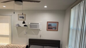 Ein Schlafzimmer mit einem Bett, einem Nachttisch mit Lampe, einem Fenster mit Jalousien und einem Deckenventilator.