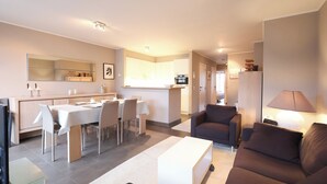 A modern living room with a sofa, a coffee table, and a dining area with chairs and a table. - Apartment Near Belgian Coastline Beach (Koksijde)