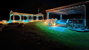 Ein überdachter Außenbereich mit Sitzgelegenheiten und einer Bühne, beleuchtet mit Lichterketten.