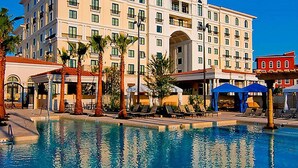 A hotel with a swimming pool, palm trees, and lounge chairs.