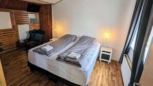 A bedroom with a bed, two bedside tables, a chair, and a wooden wall panel. - Central Apartments  (Vestmannaeyjar)