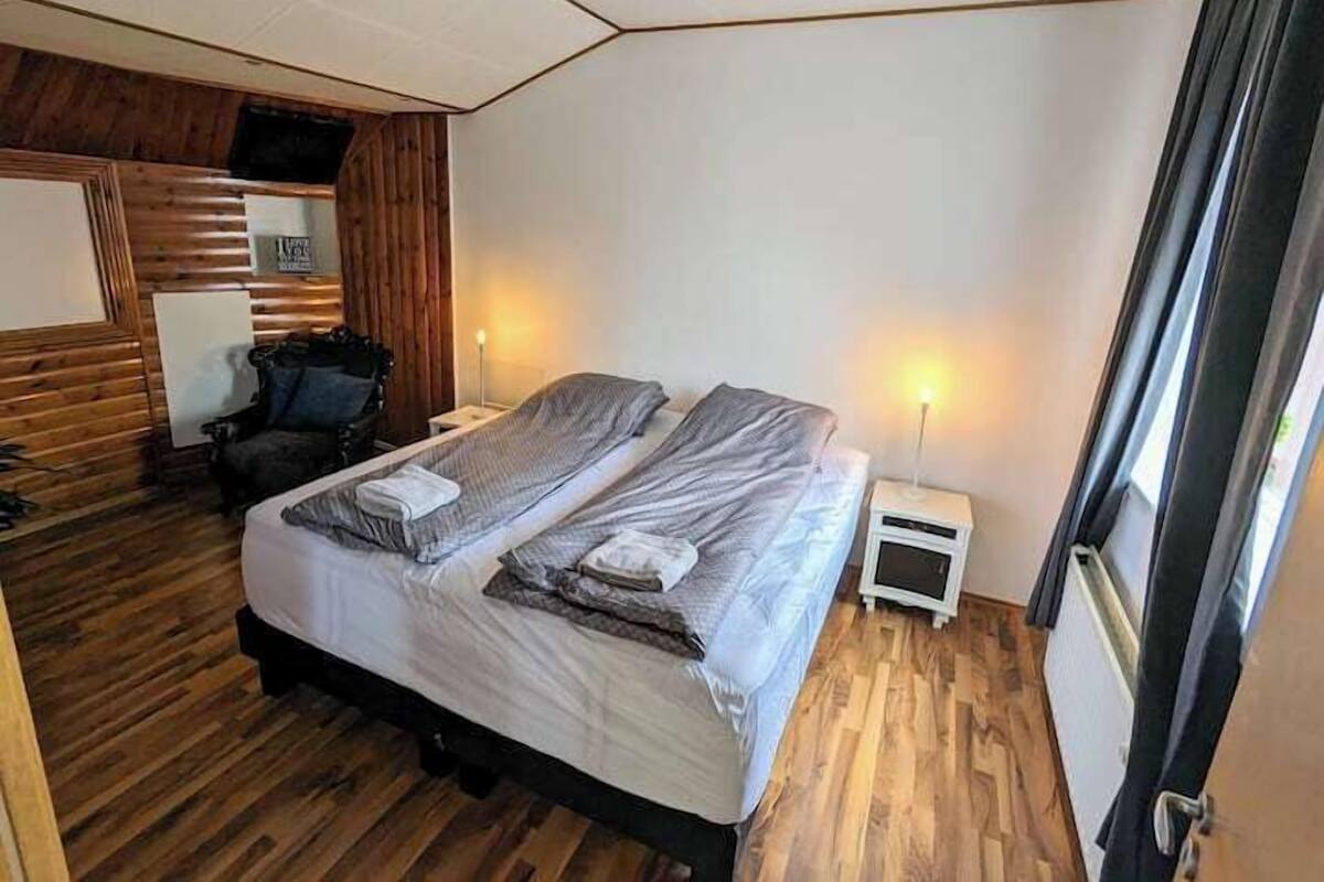 Una camera da letto con un letto, due comodini, una sedia e un pannello a parete in legno.