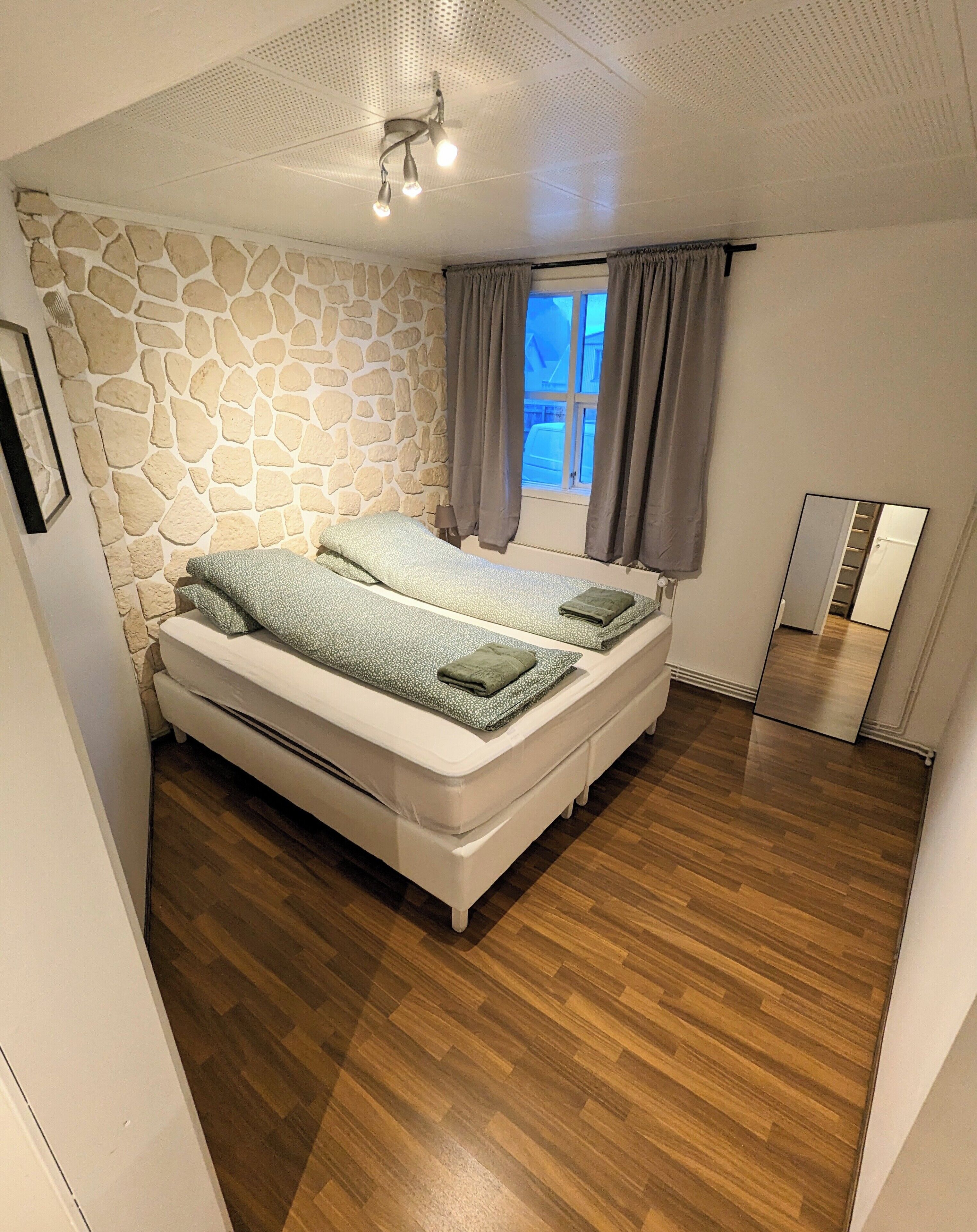Ein Schlafzimmer mit Steingemäuer, einem Bett mit grünen Handtüchern, Holzdielen und einer Deckenleuchte.