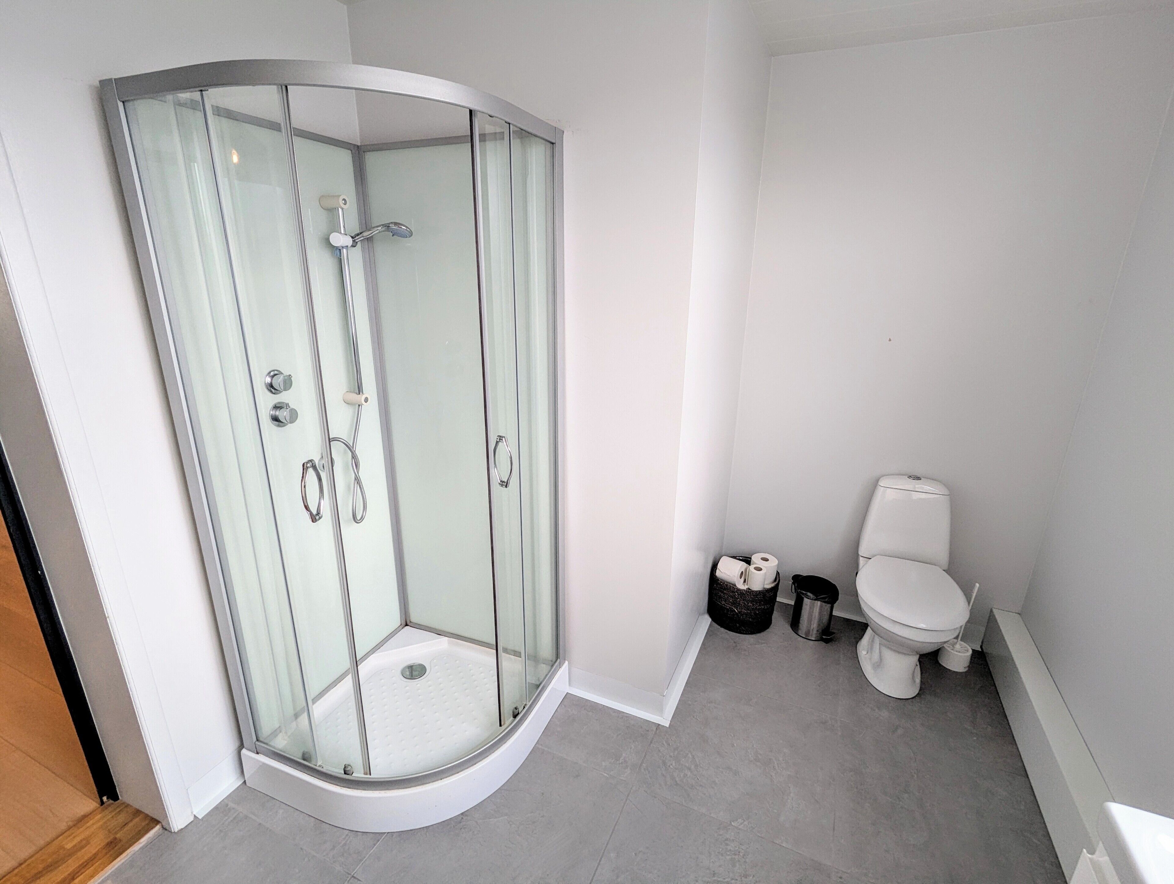 Une salle de bain moderne avec une douche à parois de verre, des toilettes et une poubelle.