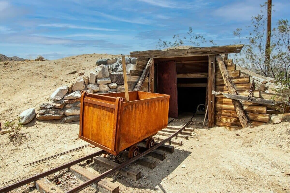 Una estructura de madera con una pequeña entrada, un carro de madera sobre rieles y un montón de rocas cerca.