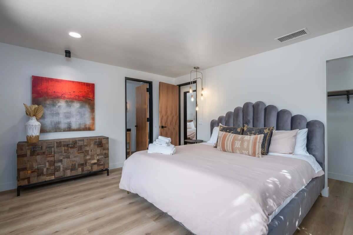 A modern bedroom with a large bed, a wooden console table, a red abstract painting, and a mirror.