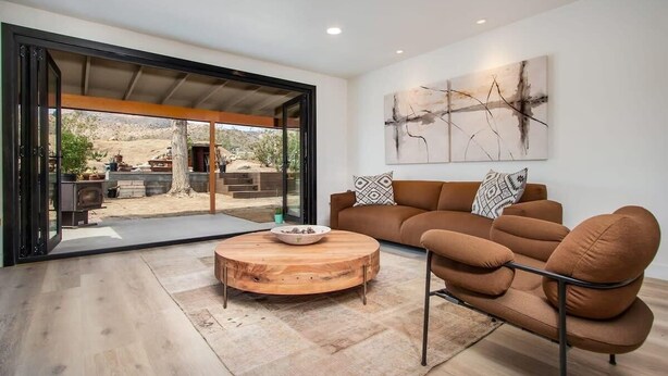 A modern living room with a brown leather sofa, a round wooden coffee table, and a large abstract painting on the wall. - @ Marbella Lane - The Wine Mine Desert Escape (Joshua Tree)
