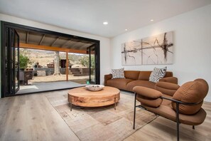 A modern living room with a brown leather sofa, a round wooden coffee table, and a large abstract painting on the wall. - @ Marbella Lane - The Wine Mine Desert Escape (Joshua Tree)