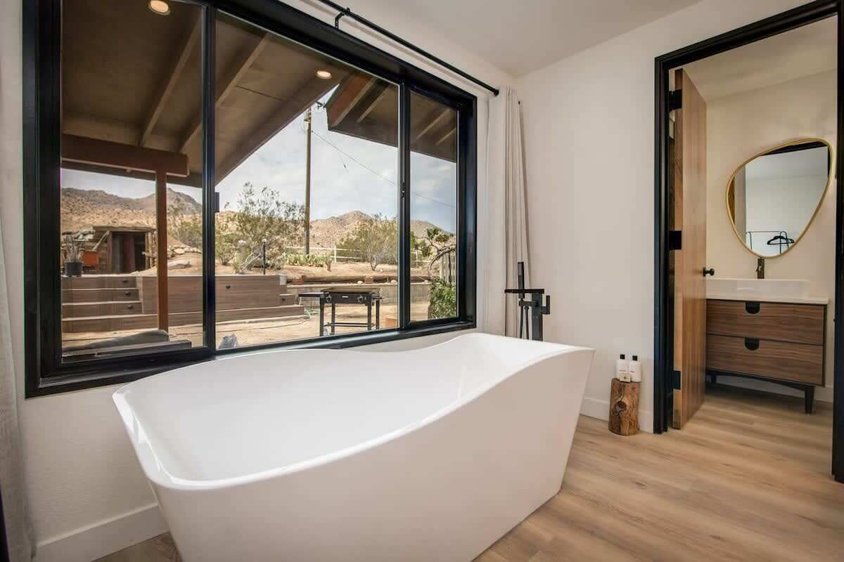 A modern bathroom with a freestanding bathtub, large windows, and a view of the desert landscape.