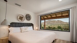 A bedroom with a large bed, a view of a desert landscape, and a modern ceiling design. - @ Marbella Lane - The Wine Mine Desert Escape (Joshua Tree)