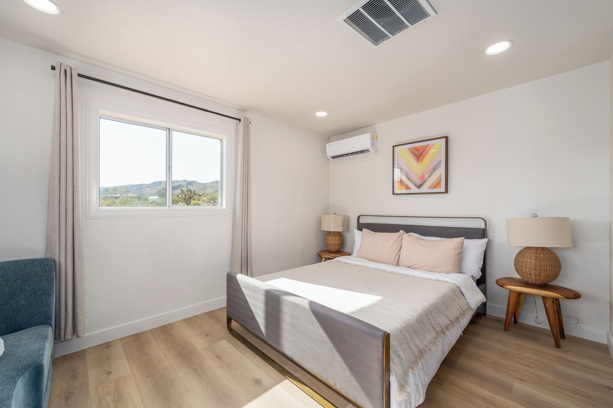 Une chambre à coucher avec un lit, deux tables de chevet, une fenêtre, un climatiseur et un tableau au mur.