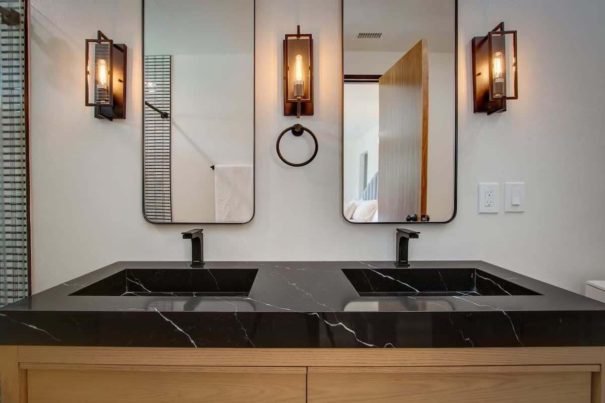 A modern bathroom with two sinks, a large mirror, and wall-mounted sconces.