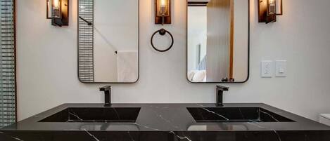 A modern bathroom with two sinks, a large mirror, and wall-mounted sconces.