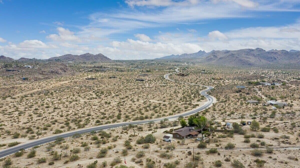 A desert landscape with a winding road, sparse vegetation, and distant mountains.